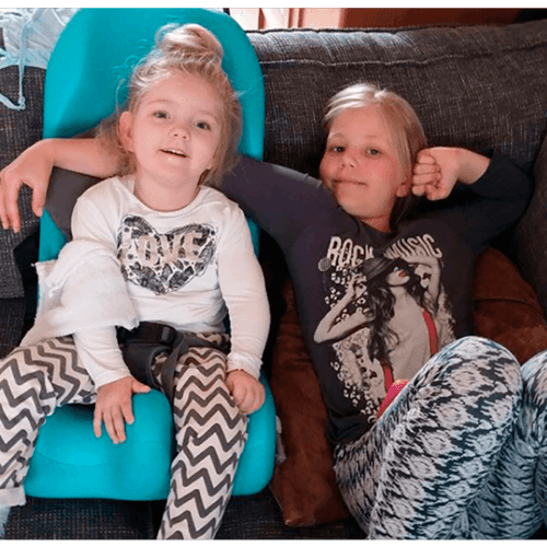 Ines relaxing on the couch in her sitter seat with her sister